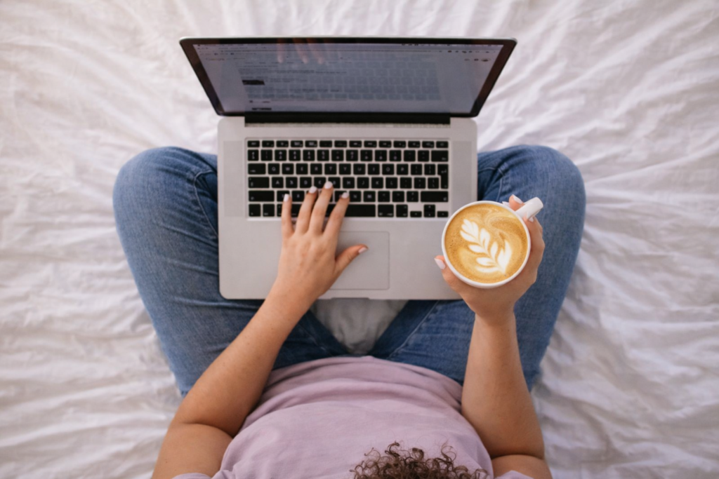 Overhead photo of a woman with a laptop on her lap and a latte in one hand